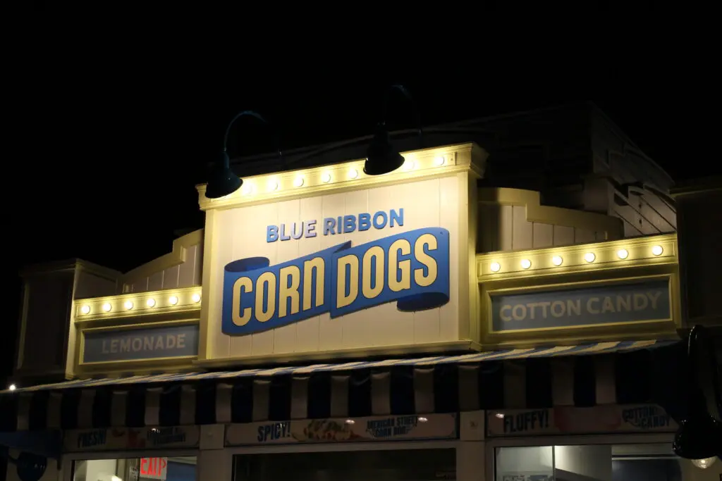 Blue Ribbon Corn Dogs sign in yellow with blue writing at night.