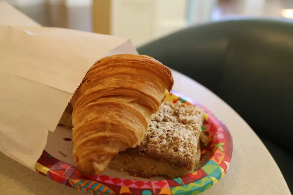 A croissant and a piece of crumb cake on a paper plate.