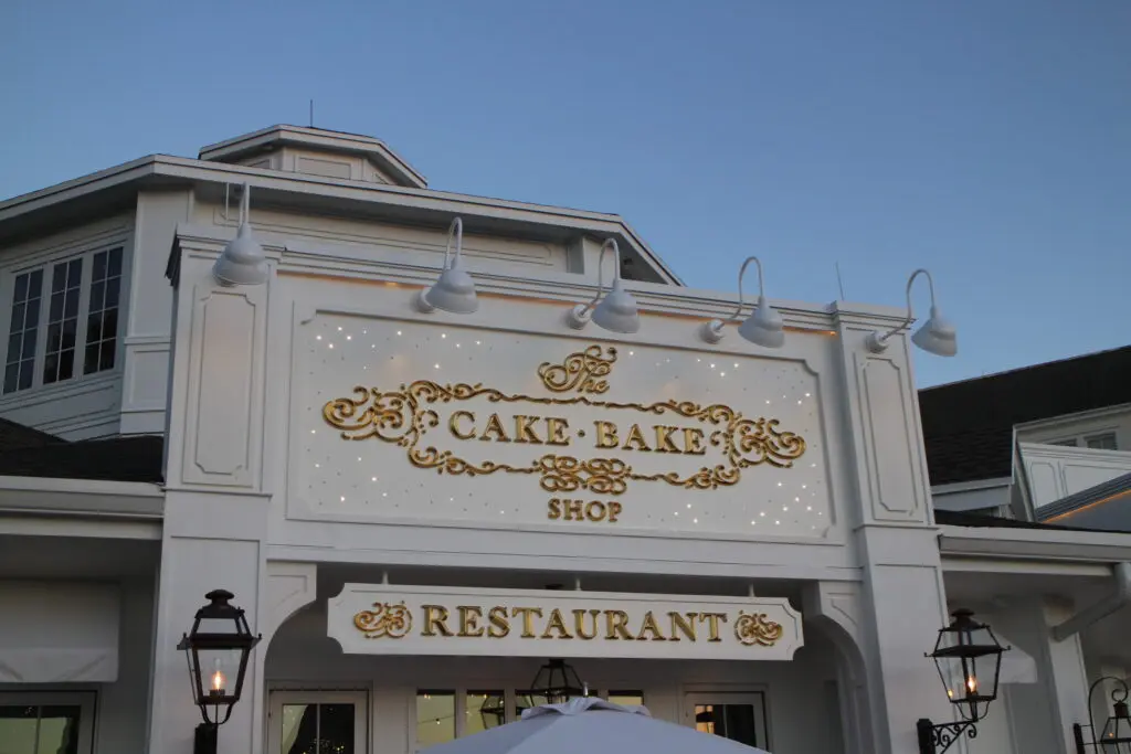 White restaurant exterior with The Cake Bake Shop in gold writing with twinkly lights.