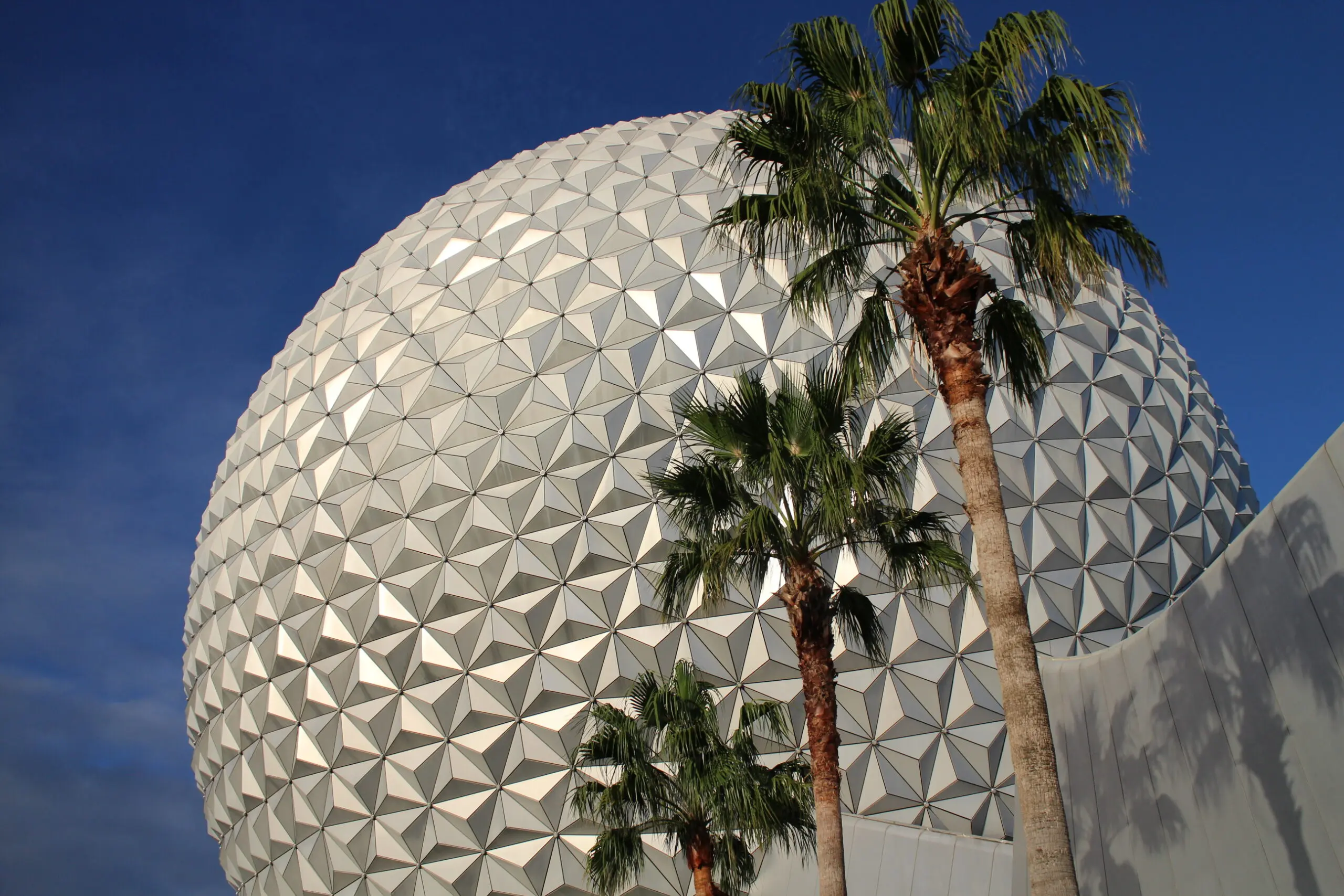 The silver Spaceship Earth round building with palm trees in front of it. This is one of the longest running Disney World rides.