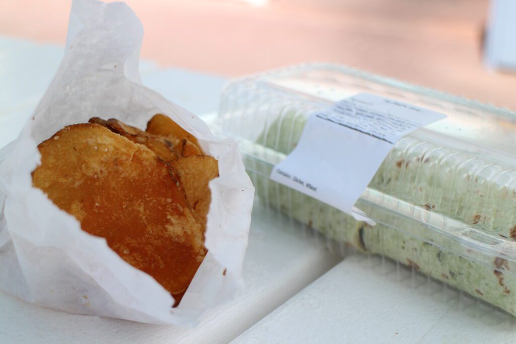 Housemade Disney chips in a white wrapper on a white picnic table with a veggie wrap in a plastic box behind them.