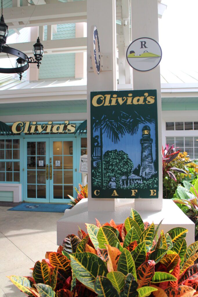 Olivias Cafe entrance with a sign and lush tropical landscaping.