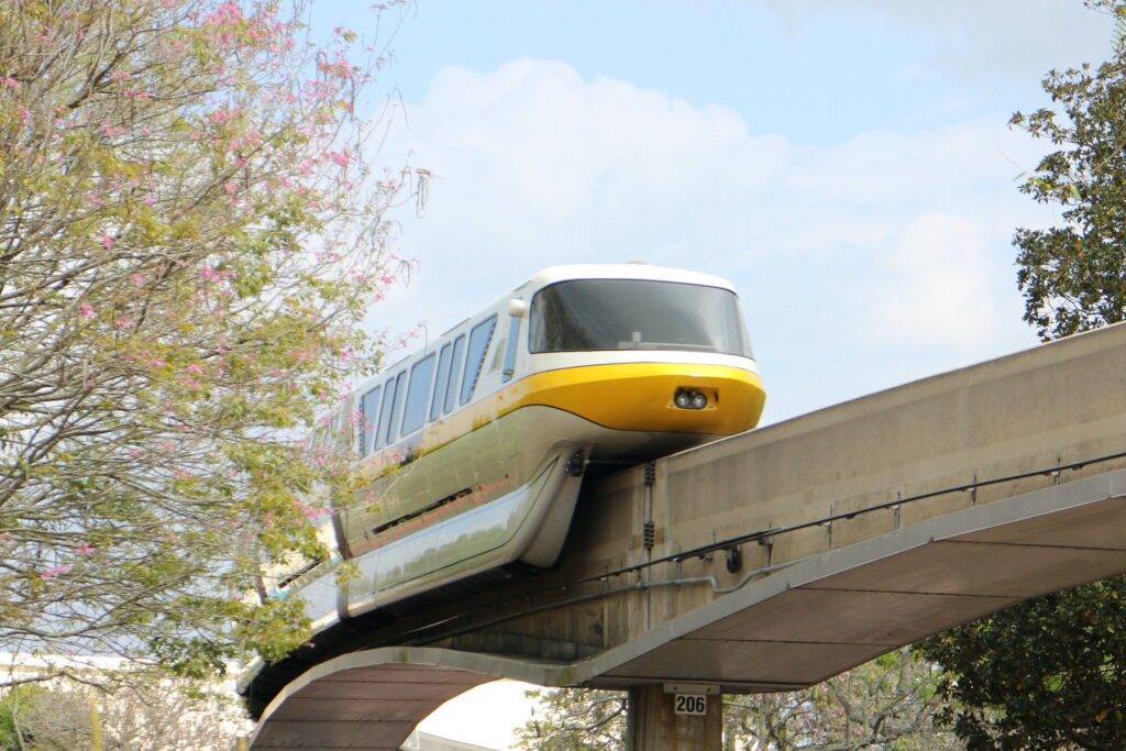 A yellow monorail cruises on a beam with a tree with pink flowers on it. The best time to visit Disney World for nice weather is around November through February.