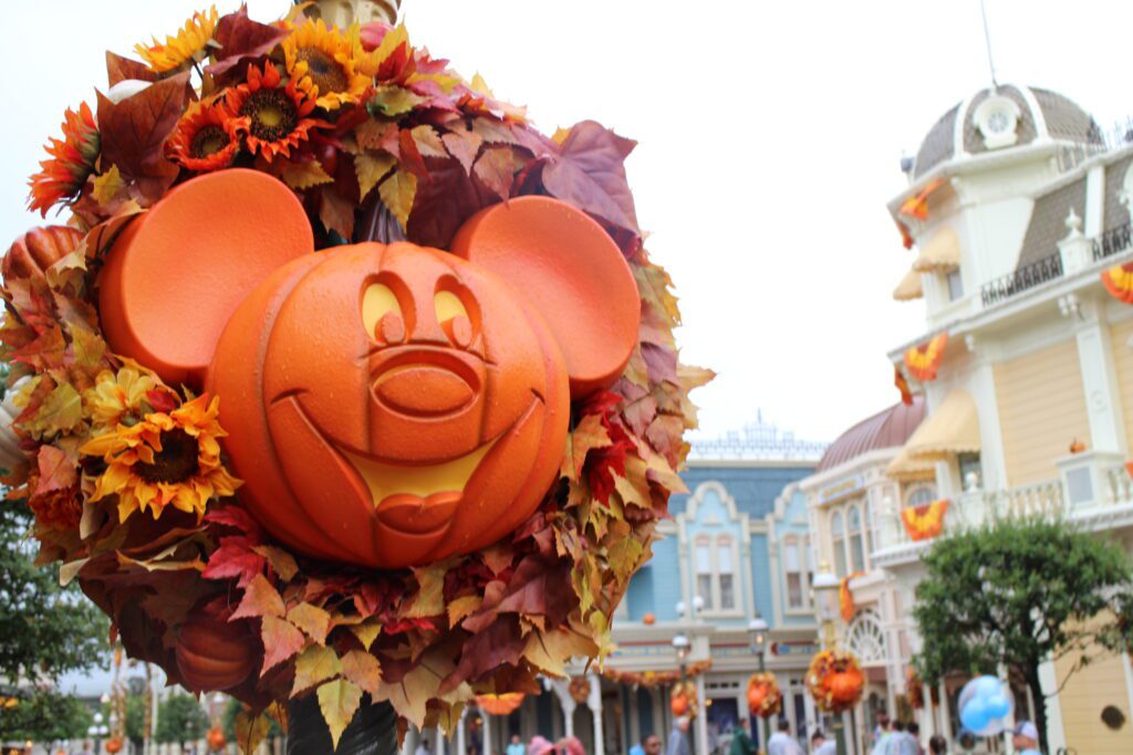 A smiley Mickey pumpkin hangs inside a fall wreath on a lamp post on Main Street with similar decorations on buildings in the background. Fall is one of the seasons that's the best time to visit Disney World for special decorations.