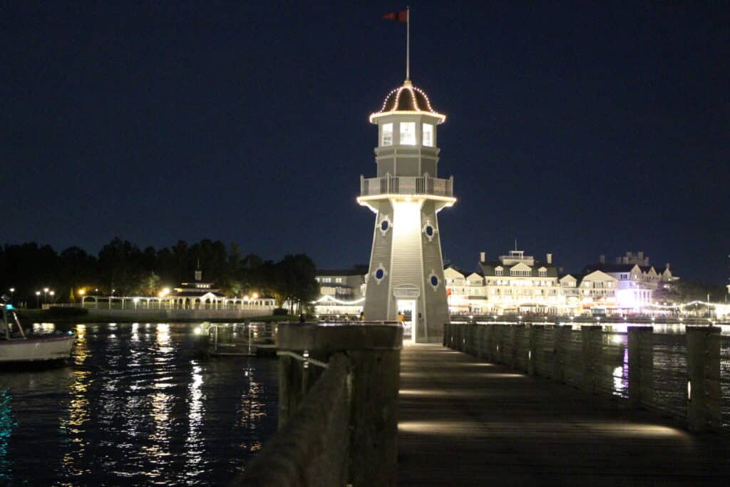 The Crescent Lake area lighthouse with Disney's BoardWalk Resort lit up across the water at night