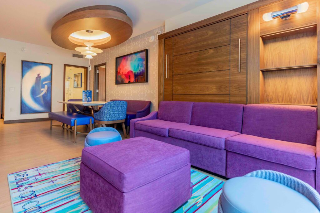 The main living space of the two bedroom Disneyland Hotel DVC villa that's themed to Fantasia with a purple couch and orchestra wall art