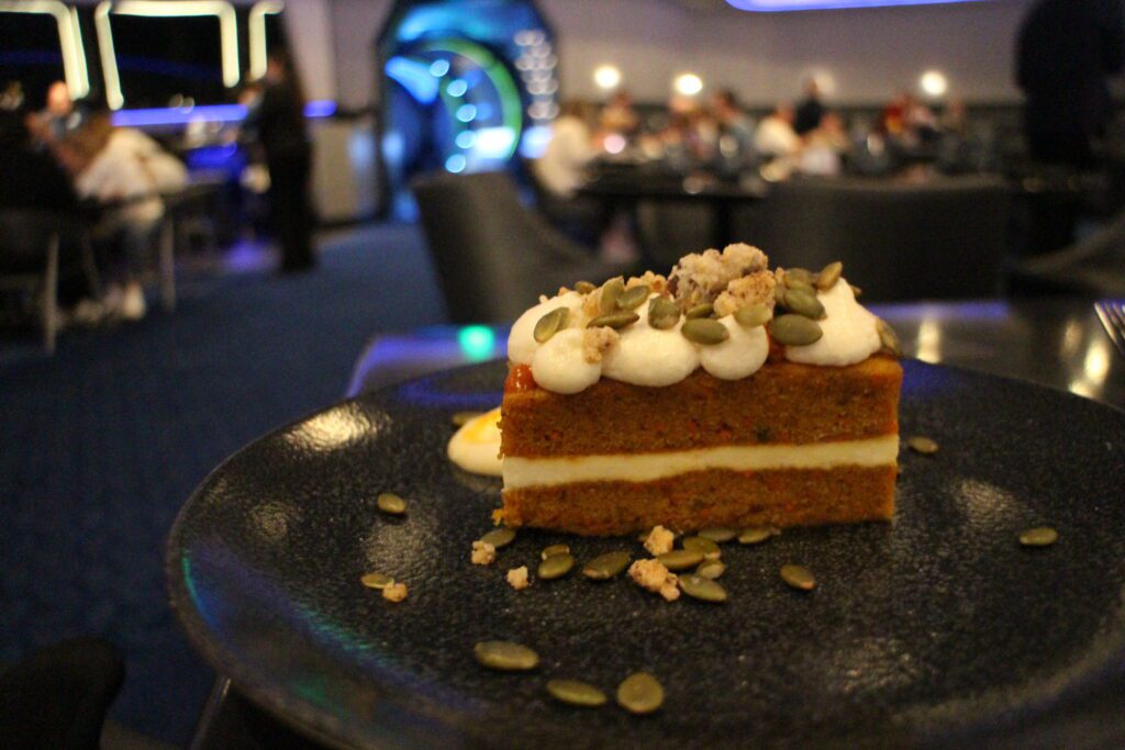 a rectangular piece of carrot cake with a space themed restaurant out of focus behind it