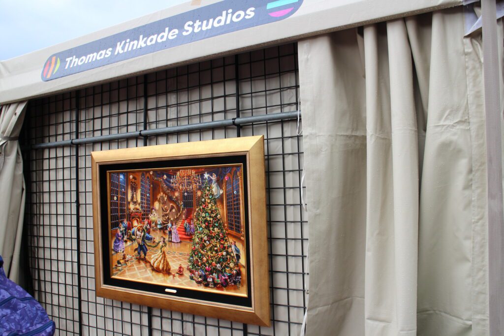 A Beauty and the Beast Christmas piece in a gold frame by Thomas Kinkade Studios hangs on the outside of a festival tent