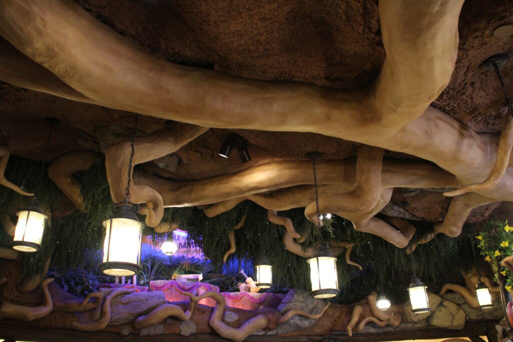 The ceiling inside Critter Co-Op, the store outside of Tiana's Bayou Adventure, covered in large tree roots and lanterns with a bayou style greenery.