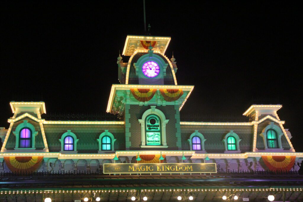 The entrance of Magic Kingdom's train station at night, adorned with fall banners and lit in Halloween colors of green and purple.