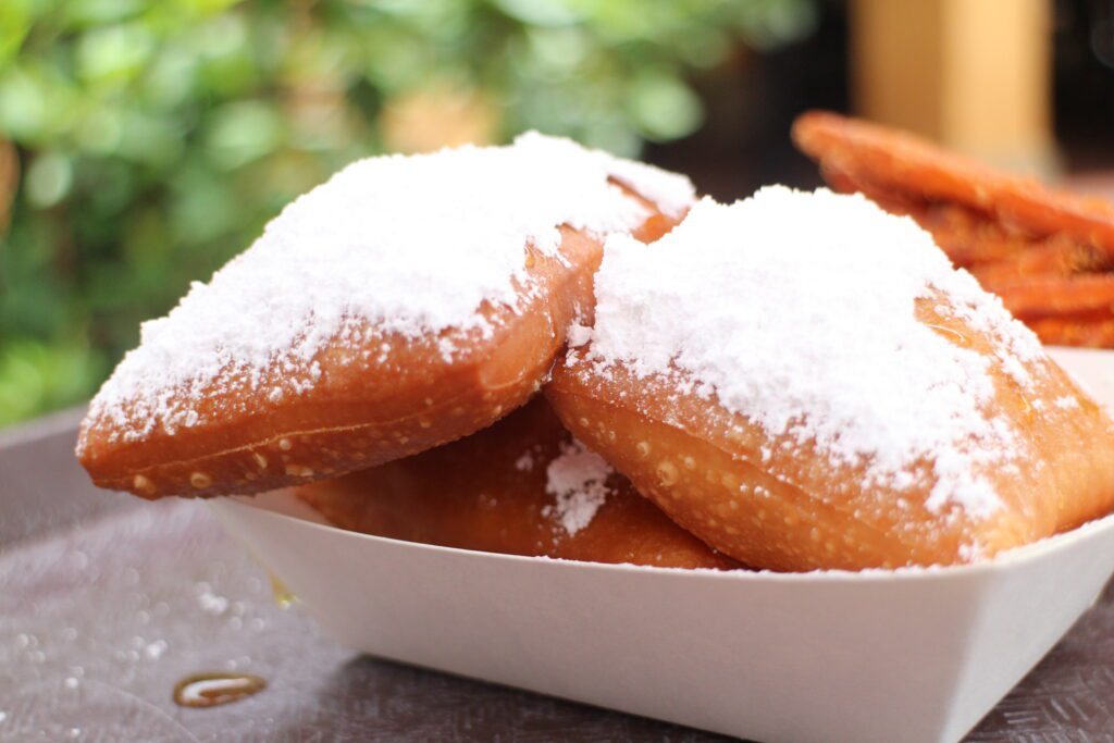 Big, puffy beignets covered in powered sugar and honey at Disney World near Tiana's Bayou Adventure.