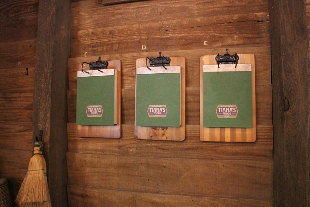 Clipboards hanging on a wood plank wall with papers that say Tiana's Bayou Adventure.