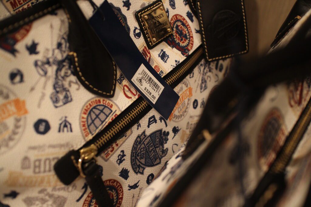 A close up of a Disney Vacation Club Dooney and Bourke large tote found in the DVC store at Riviera that's white with blue and yellow art.