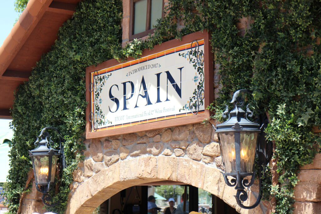 A white sign that reads Spain in black surrounded by greenery on the Epcot International Food and Wine Festival booth.