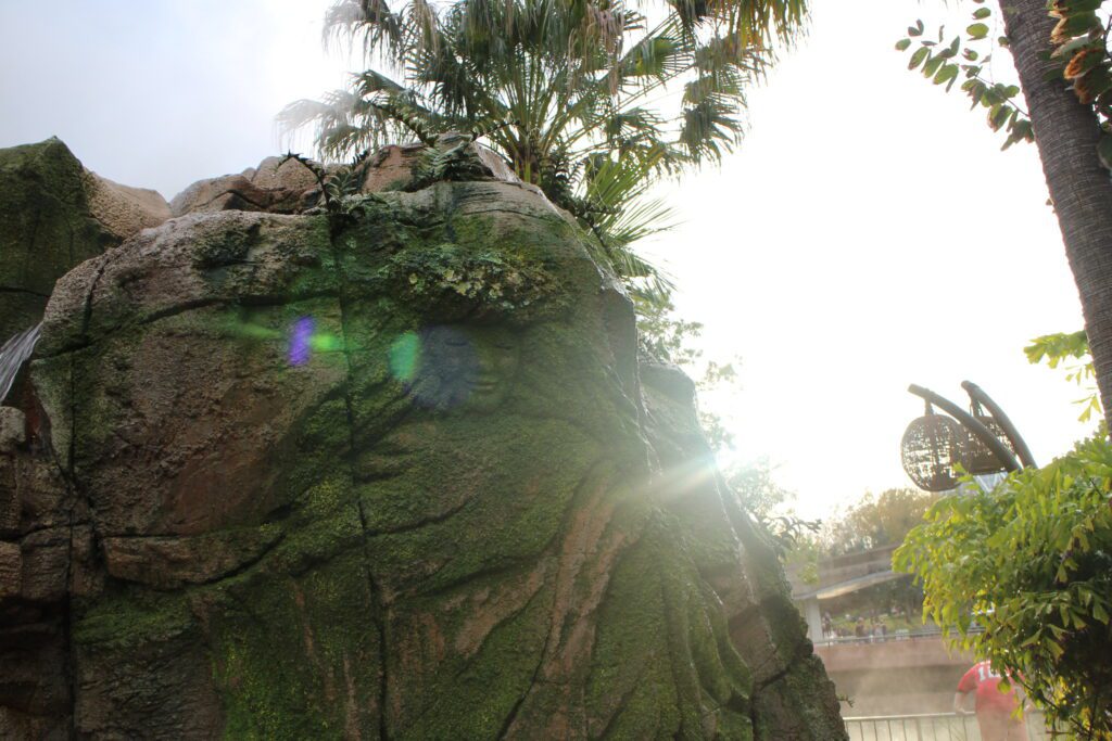 A Moana style girl carving on a mossy, green rock with a ray of sun shining over it.