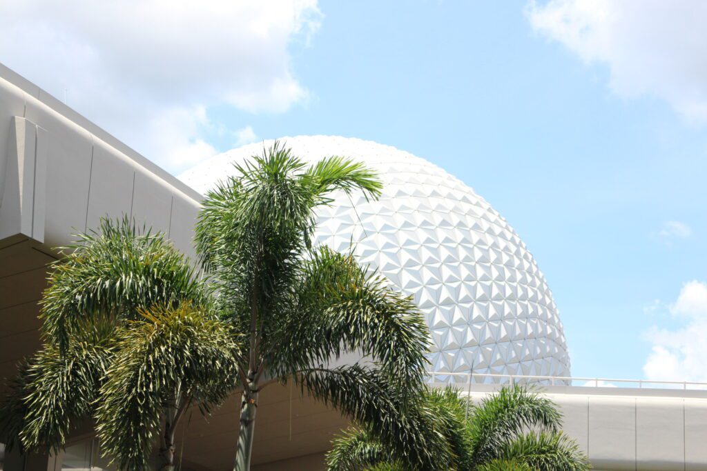 A sunny Florida day with a blue sky, palm trees and the top of the Spaceship Earth attraction peeking through.