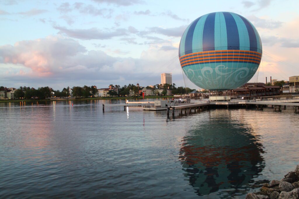 A balloon attraction floats over a lake during sunset, showcasing the kind of view you might have for drinks on the water at Disney World if you dine at Disney Springs.