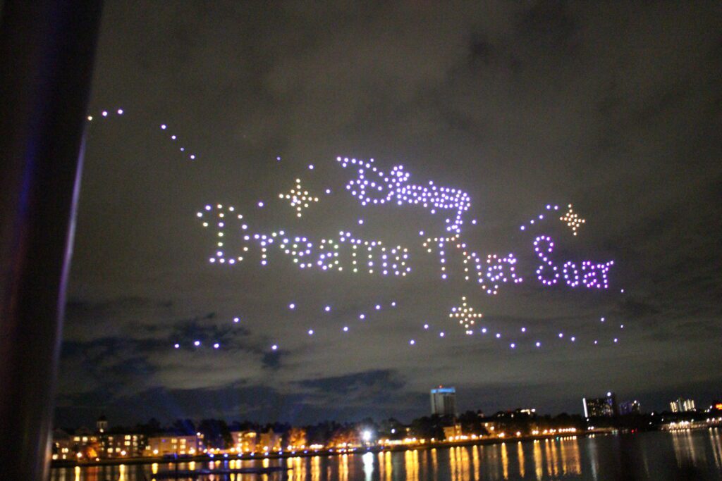 Disney Dreams That Soar is spelled out in the night sky using light up drones in purples and yellows.