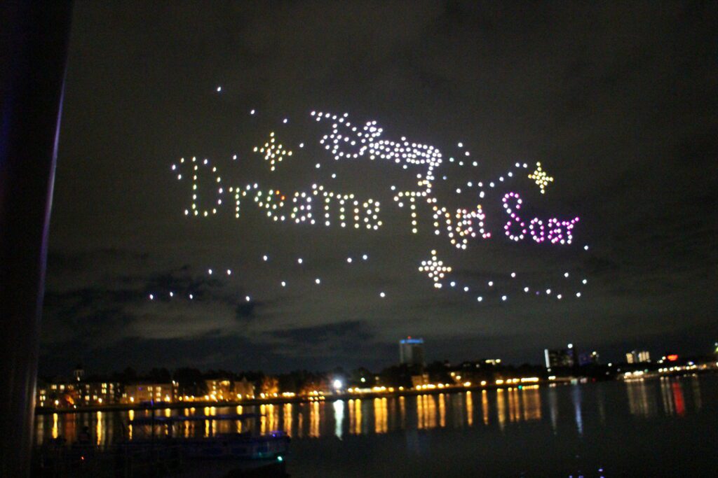 Disney Dreams That Soar spelled out in drones in the sky at night surrounded by pixie dust.