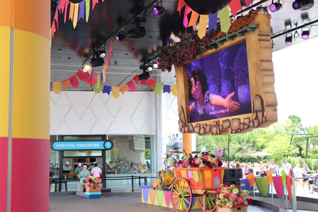 The Encanto singalong show stage, outdoors with colorful flags strung. Disney World news July 2024