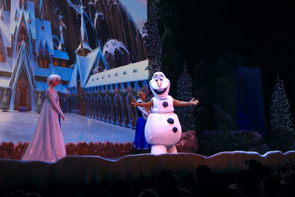 Olaf greets the audience with Elsa and Anna behind him at the Frozen singalong at Disney's Hollywood Studios.