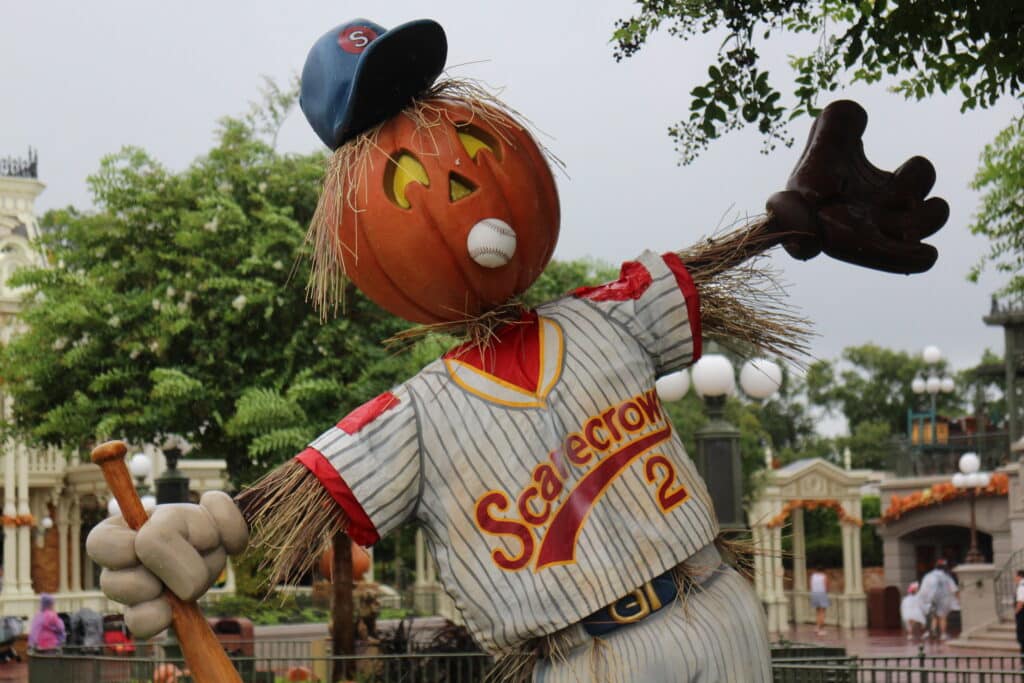 A scarecrow with a pumpkin head wears a baseball outfit on Main Street USA at Magic Kingdom. This is part of the Disney World fall decorations.