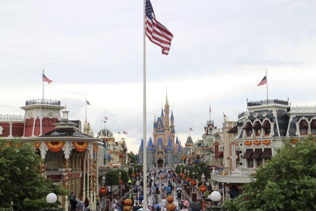 A flag pole stands over the Town Square of Magic Kingdom, looking down Main Street where the Disney World fall decorations of pumpkins and orange bunting line the shops.