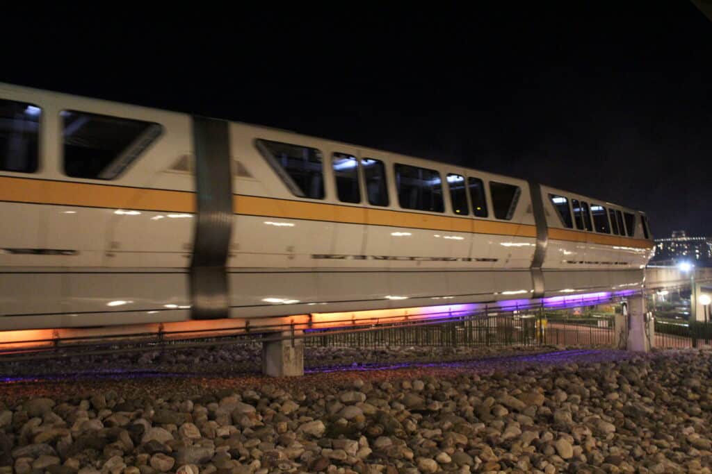 A monorail rides by at night, lit up orange and purple underneath for Disney World fall decorations.