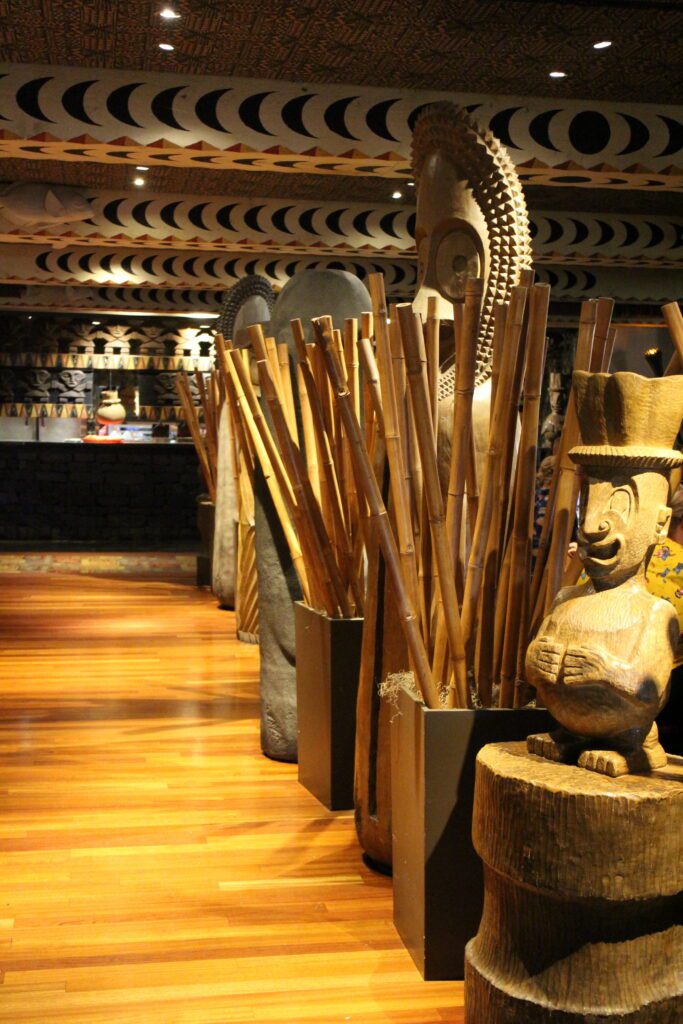 The entry of the Ohana Polynesian restaurant with wood floors and tikis lining a walkway.