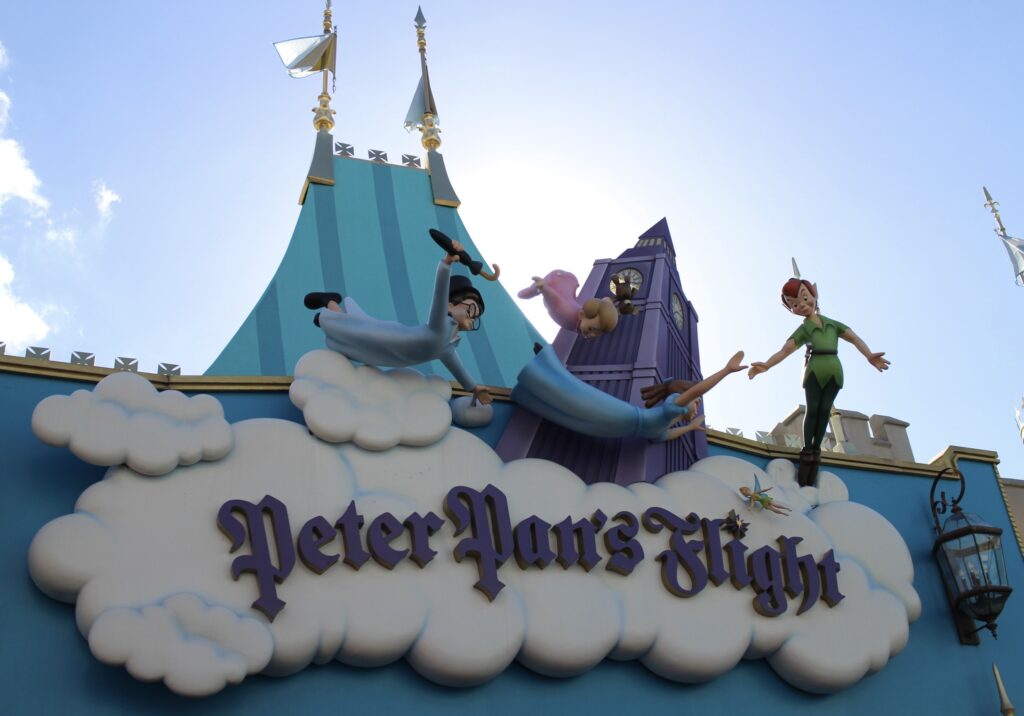 The colorful sign of Peter Pan's Flight written in a pointy, vintage font on a cloud surrounded by Peter and the Darling children.