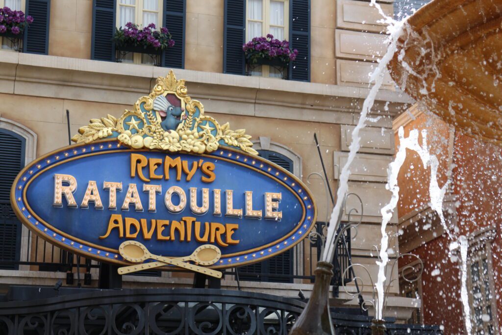 The Remy's Ratatouille Adventure sign at Epcot is blue with gold accents, set in a fancy French style.