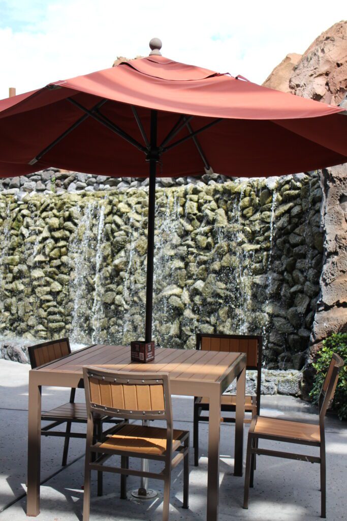 An outdoor table and chairs under an umbrella in front of a waterfall.