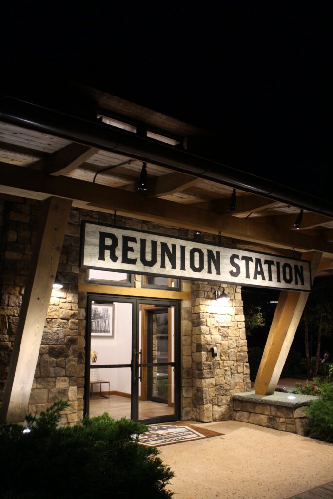 It's night time at Reunion Station, a craftsman style building with a clear door and stone front.