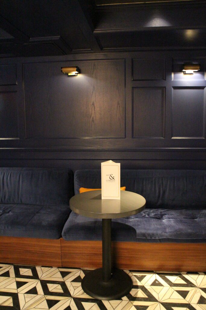 A booth seating wall that's navy blue with busy, triangle tile floor at Ale and Compass Lounge.