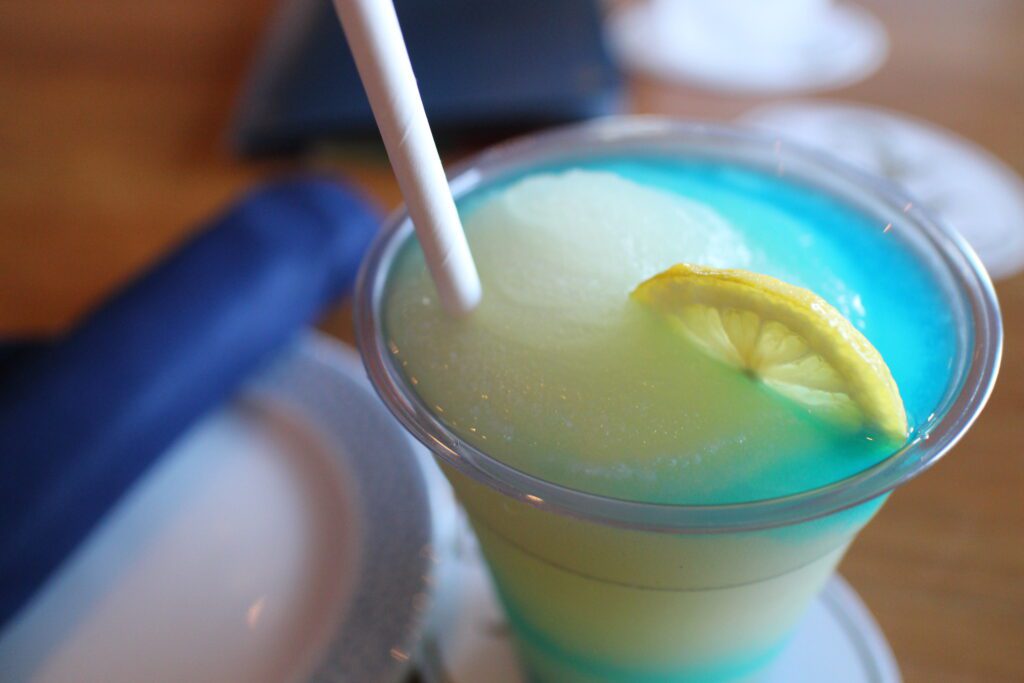 A Bar Riva Mediterranean Wave drink, icy green and blue, with a think, lemon slice in it.