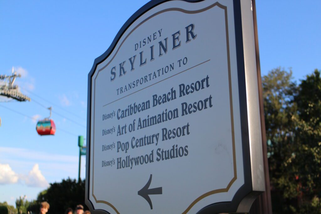 Disney Skyliner resorts sign with gondolas flyinh in the background.