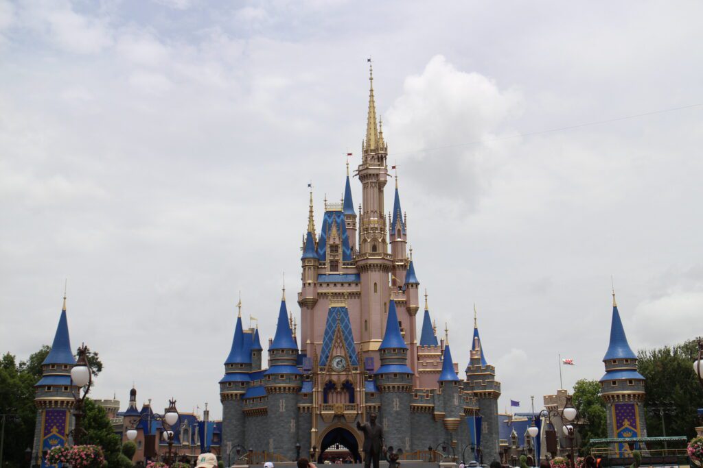 The pinkish Disney World castle with blue roofs in front of cloudy white sky.