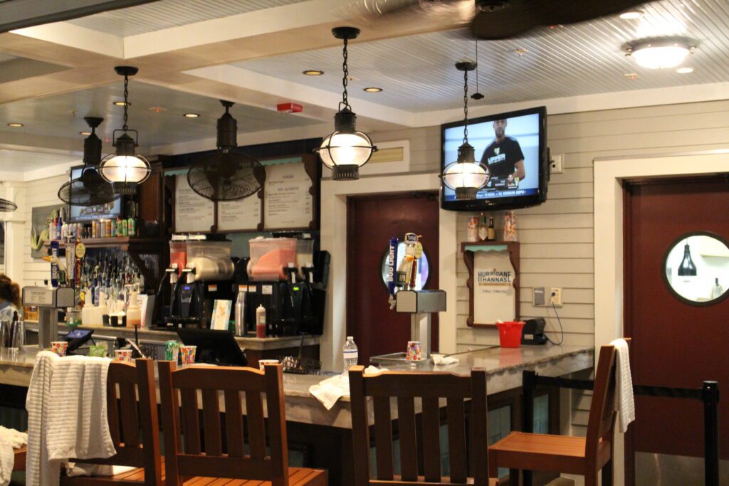 Hurricane Hanna's Waterside Bar and Grill outdoor bar with wooden stools, a television and nautical lamps.