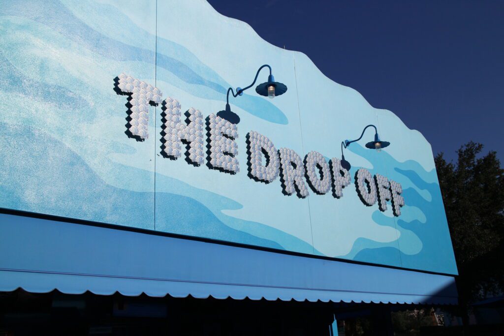 The Drop Off pool bar sign at Disney's Art of Animation Resort. It's spelled out in silvery blue fish, like the film, and has a blue ocean looking background.