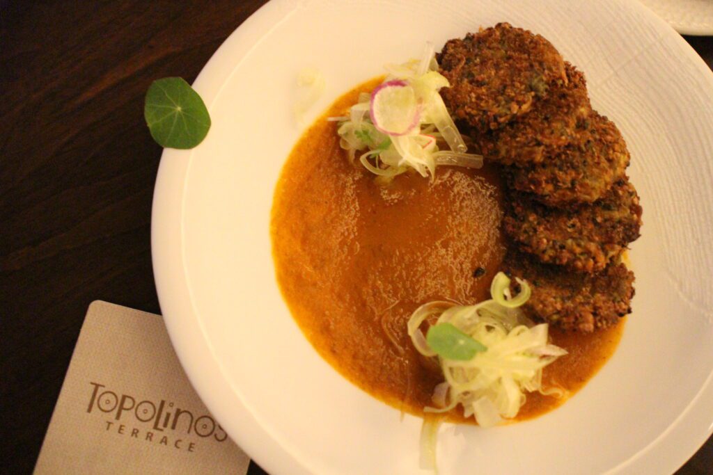 Topolino's Terrace round Ratatouille Fritters on a white plate with light red sauce.