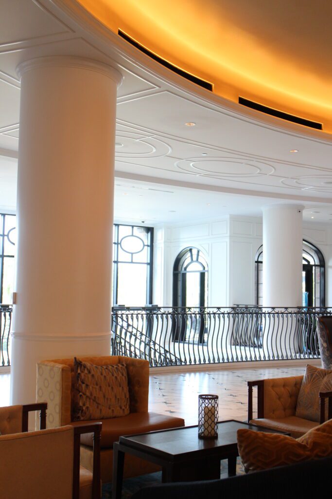 Disney's Riviera Resort lobby is simple with a white ceiling, large window over looking the property, a black railing and some chairs pictured.