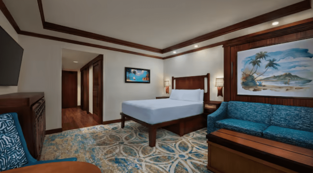 Inside an original Polynesian Deluxe Studio there is white walls with dark floors and trim, a queen size bed, a couch that has a pull down bed behind it and a pulldown bed concealed in a piece of furniture.