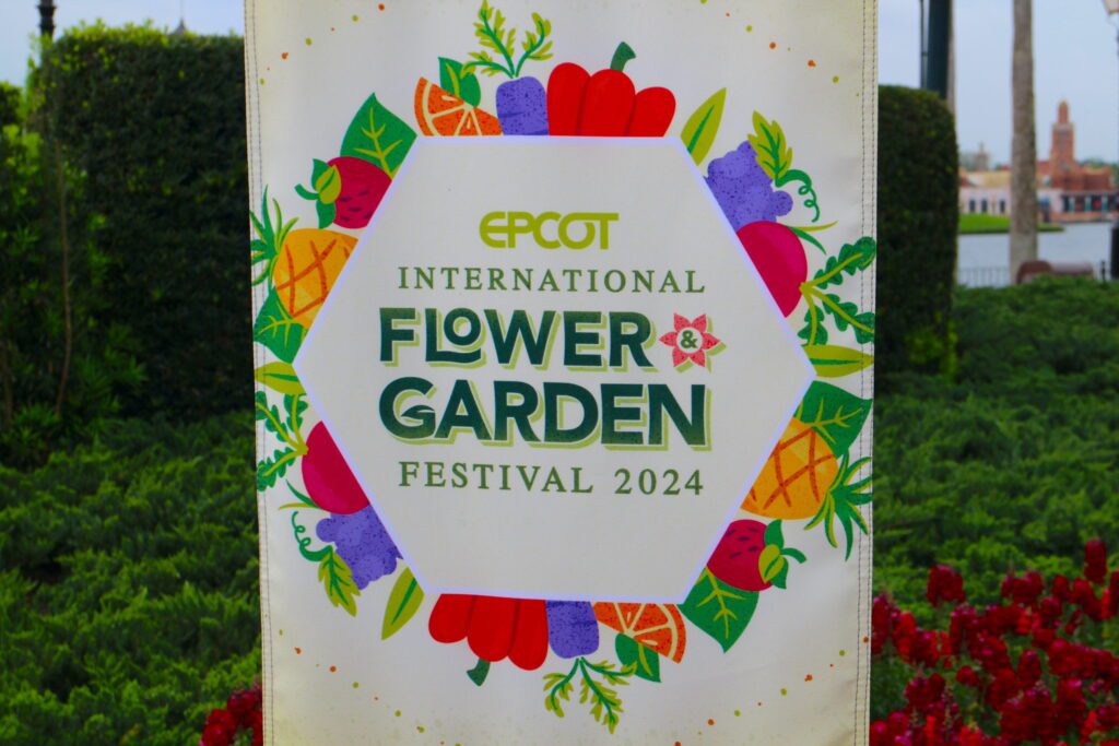 An Epcot International Flower and Garden Festival sign in front of a green area.