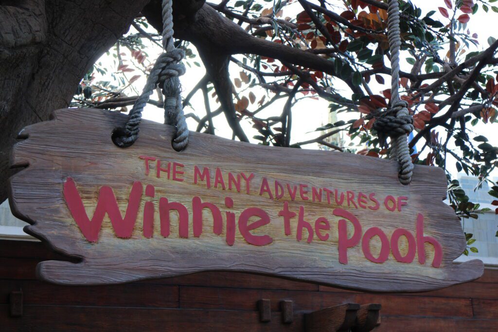 A wood style sign with The Many Adventures of Winnie the Pooh written on it outside of the attraction at Magic Kingdom.