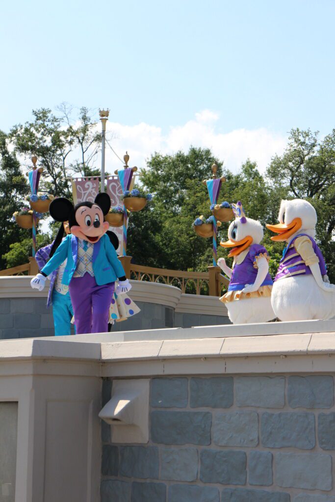 Mickey Mouse on stage at Disney World with Donald and Daisy behind him.