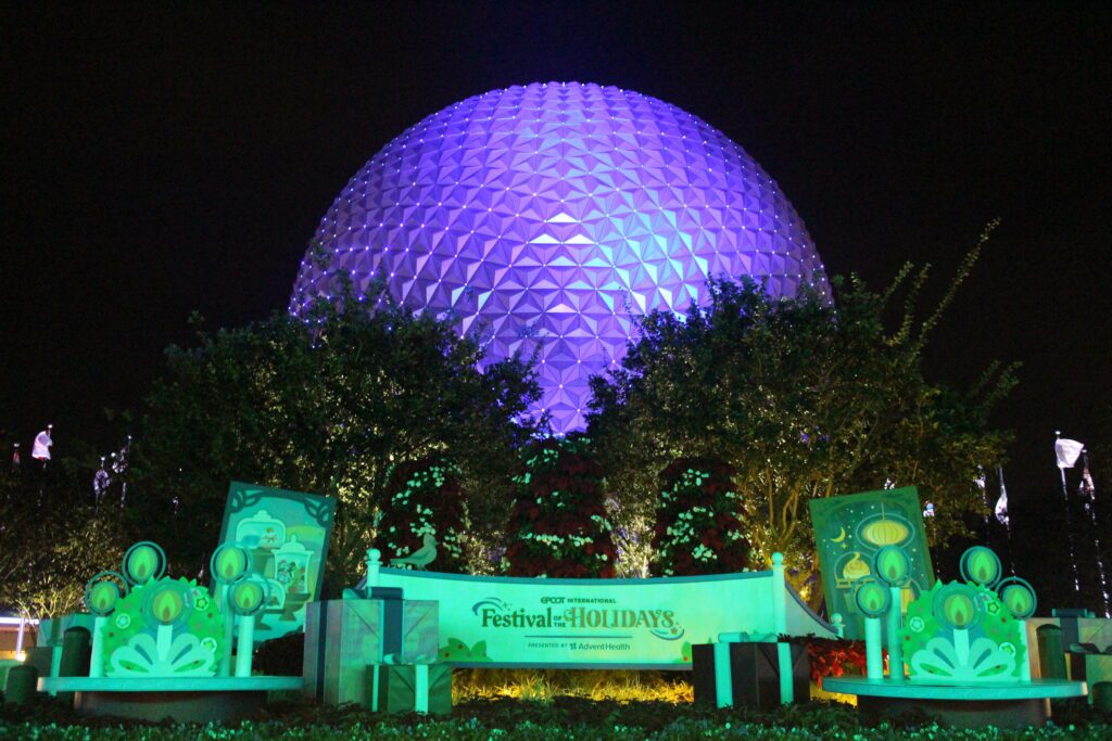 The Epcot International Festival of the Holidays entrance with a lit green sign and Spaceship Earth behind it. This is one of the best times to visit Disney World. 2025