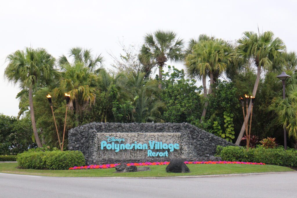 A tropical Polynesian resort entrance sign surrounded by palm trees.